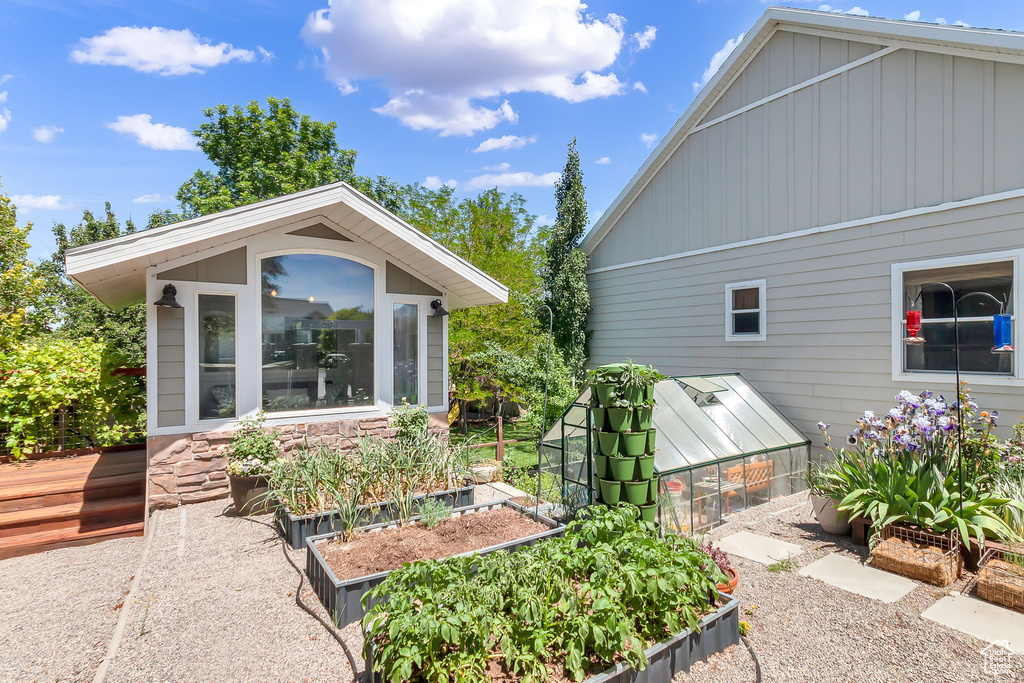 View of side of home with a garden, an exterior structure, board and batten siding, an outdoor structure, and a sunroom
