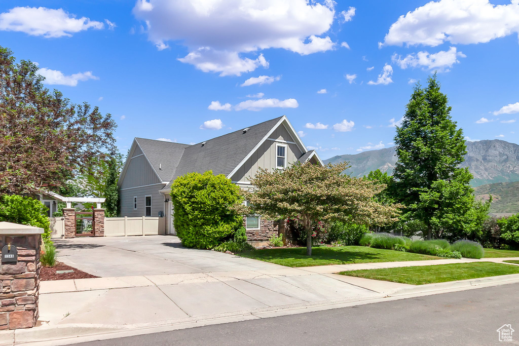 View of side of property featuring concrete driveway, a mountain view, a gate, stone siding, and board and batten siding