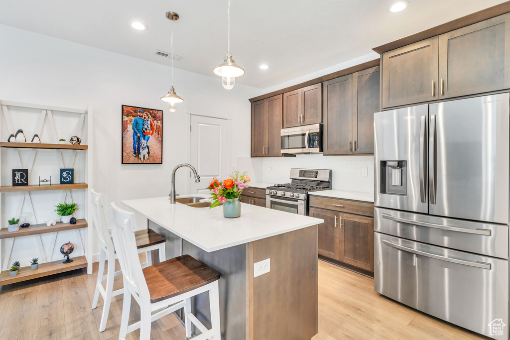 Kitchen featuring appliances with stainless steel finishes, a sink, light countertops, light wood finished floors, and a kitchen bar