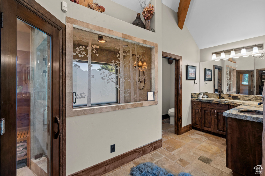 Full bathroom with baseboards, vanity, toilet, stone tile floors, and beam ceiling