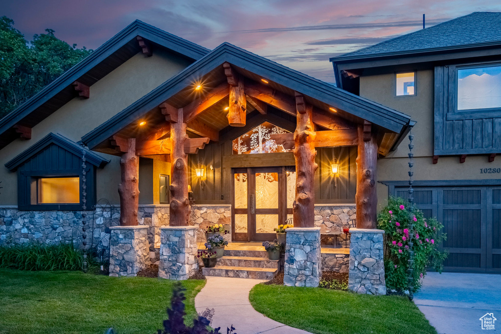 View of exterior entry with stone siding, stucco siding, a garage, and a lawn