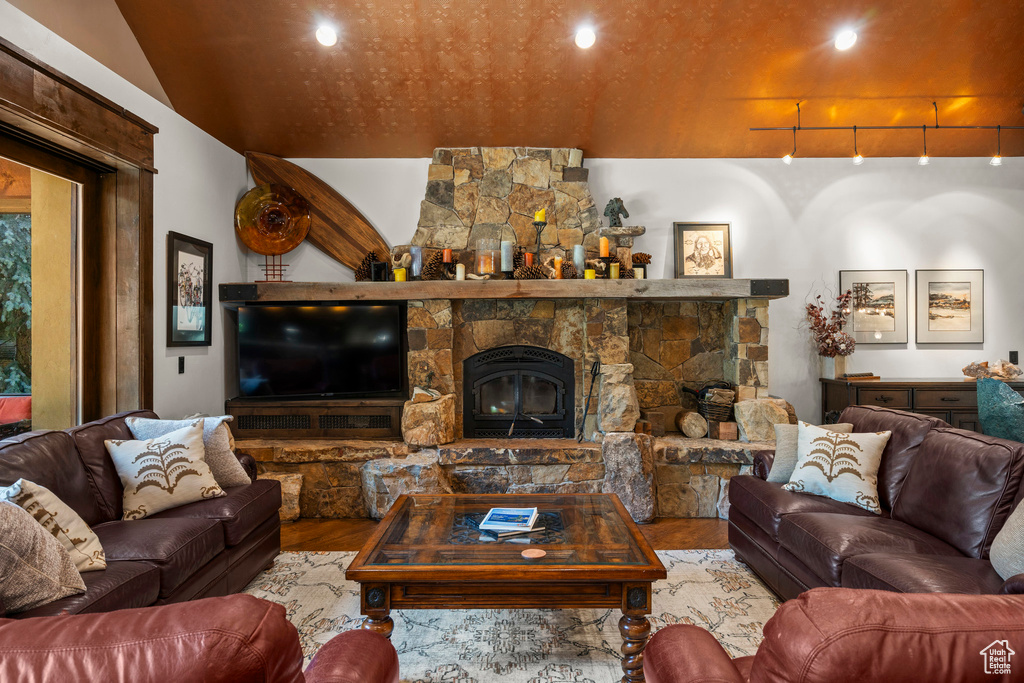 Living area featuring wood finished floors, lofted ceiling, and a stone fireplace