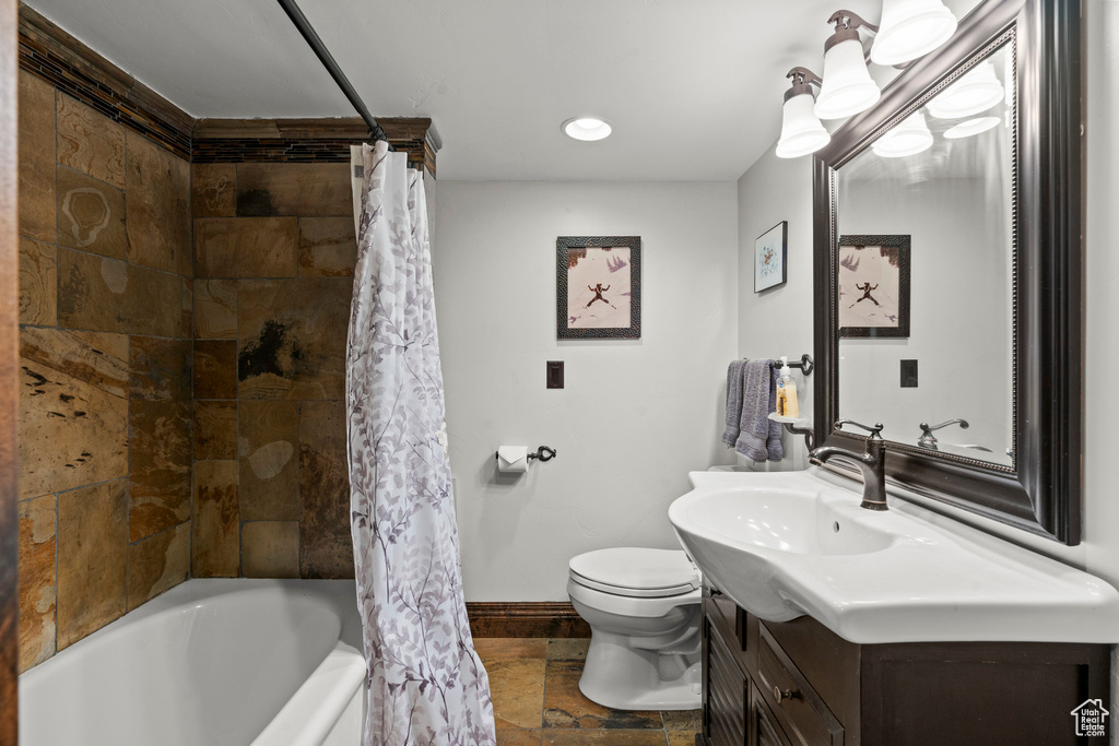 Bathroom featuring vanity, toilet, baseboards, shower / bath combo, and stone tile flooring