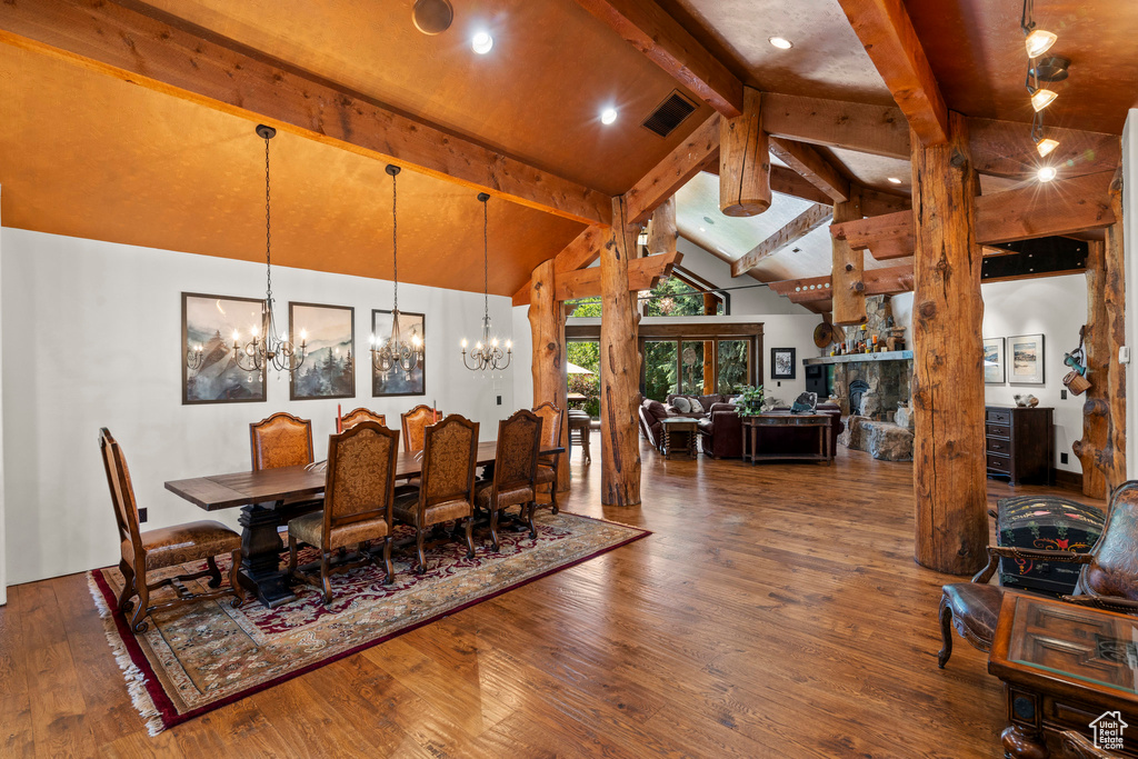 Dining space with a chandelier, beamed ceiling, wood finished floors, and high vaulted ceiling