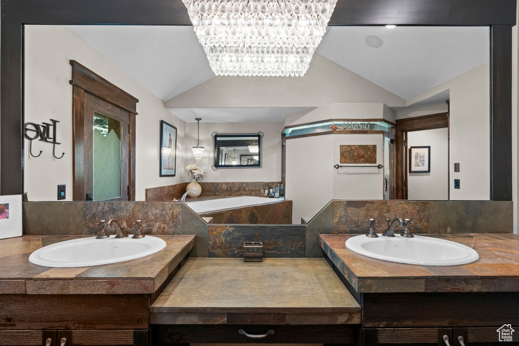 Full bathroom featuring lofted ceiling, a bath, two vanities, and a chandelier