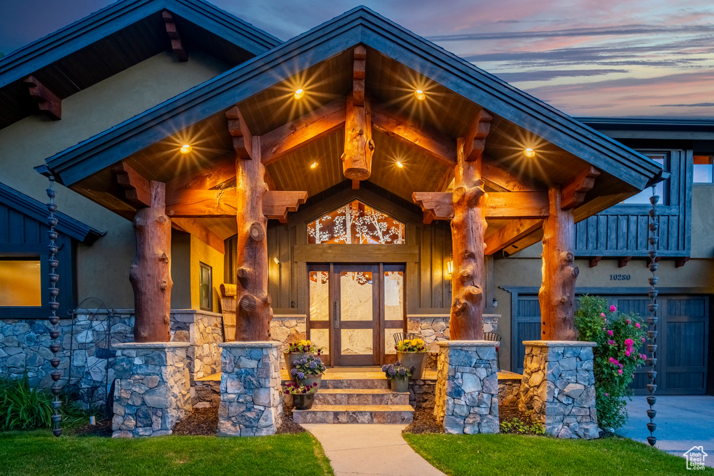 Exterior entry at dusk with stone siding, a porch, and stucco siding
