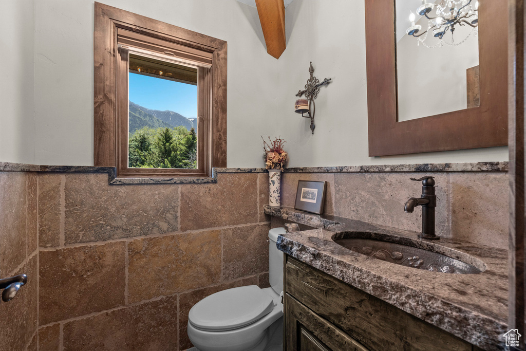 Half bathroom featuring tile walls, vanity, toilet, and wainscoting