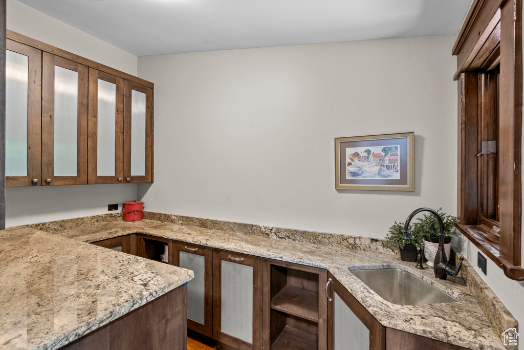 Kitchen with a sink, glass insert cabinets, dark brown cabinetry, and light stone counters