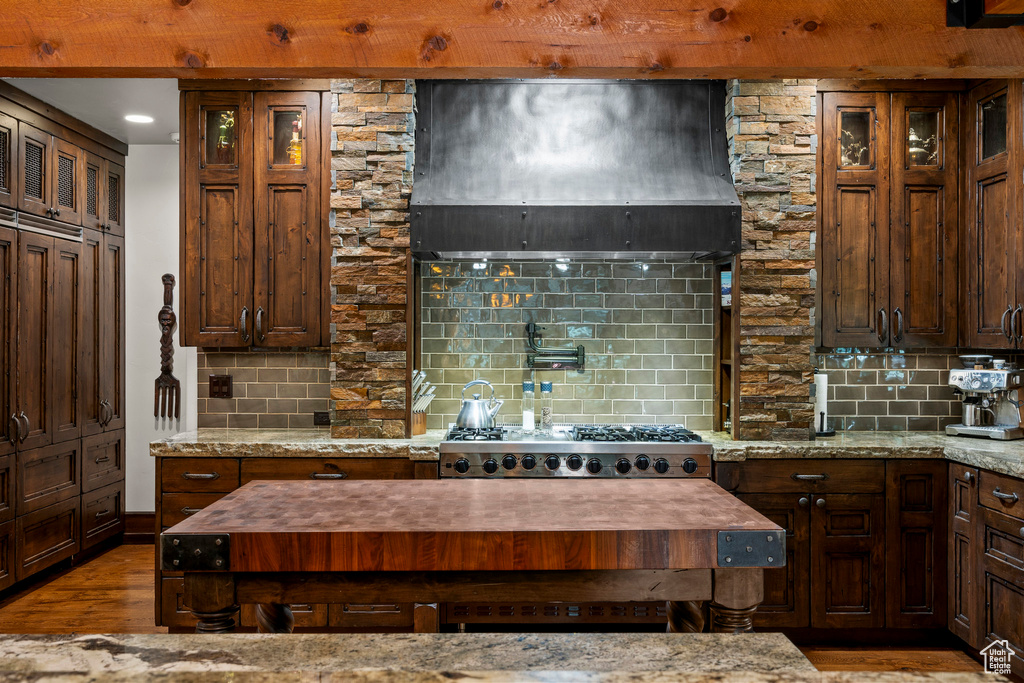 Kitchen featuring ventilation hood, backsplash, wood finished floors, and glass insert cabinets
