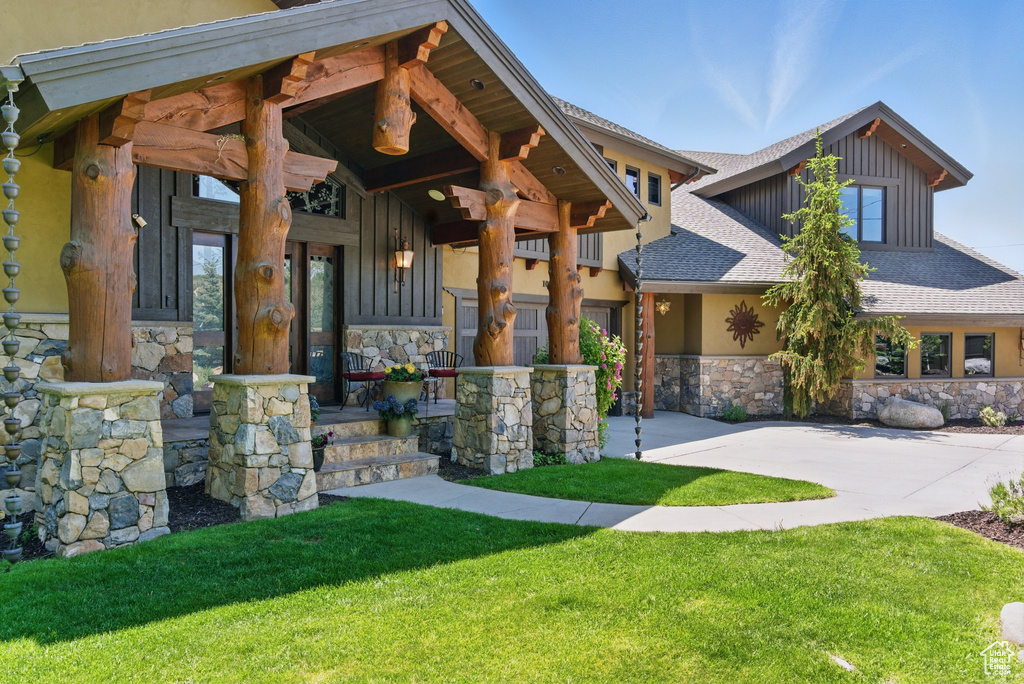View of front of property with stone siding, roof with shingles, a front lawn, stucco siding, and covered porch