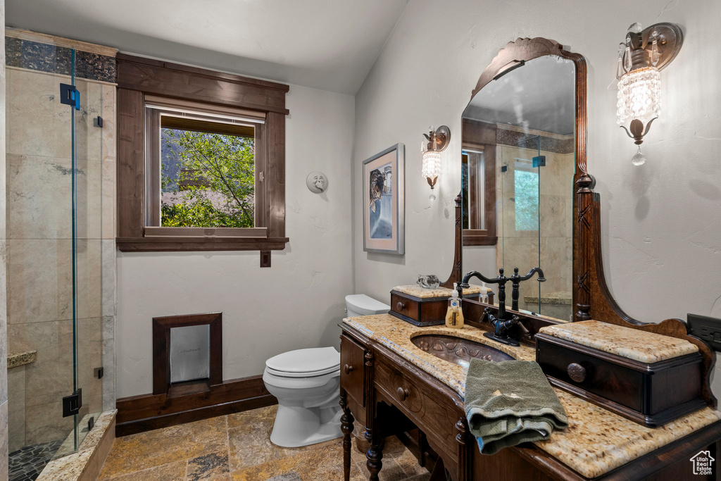 Full bathroom with stone tile floors, vanity, a stall shower, toilet, and baseboards