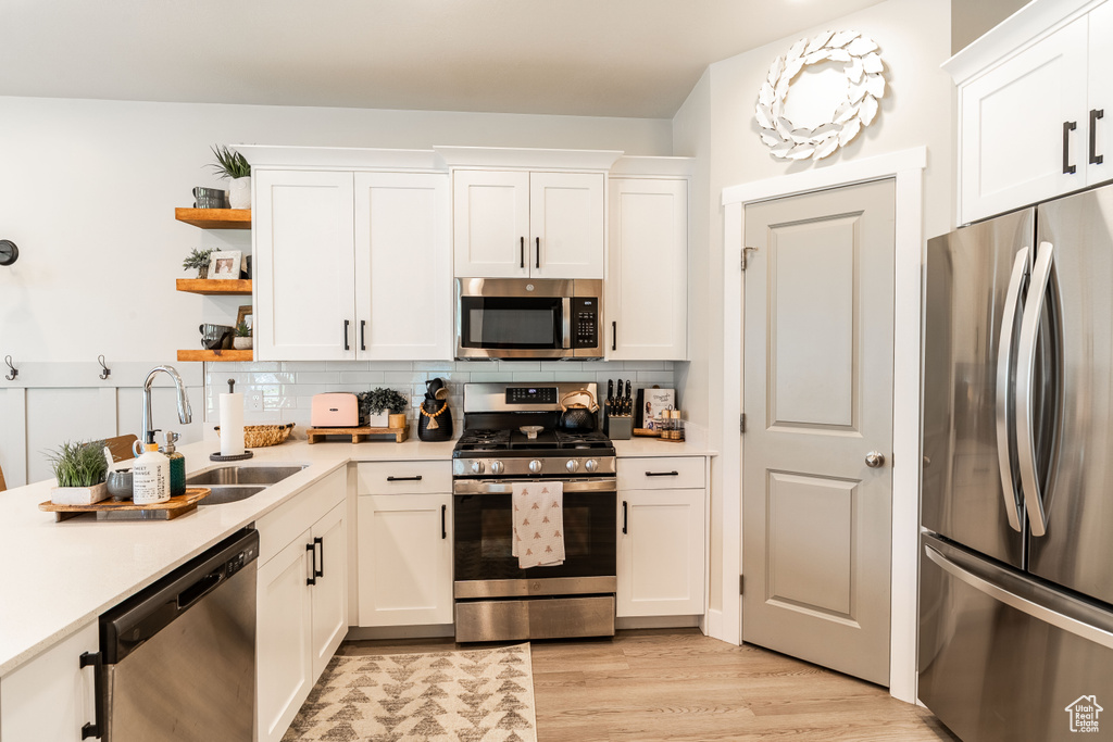Kitchen with stainless steel appliances, light countertops, white cabinets, backsplash, and open shelves