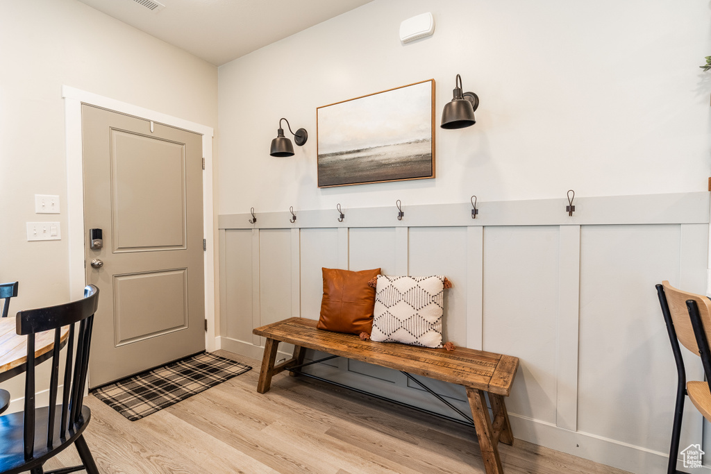 Mudroom with light wood finished floors, wainscoting, and a decorative wall