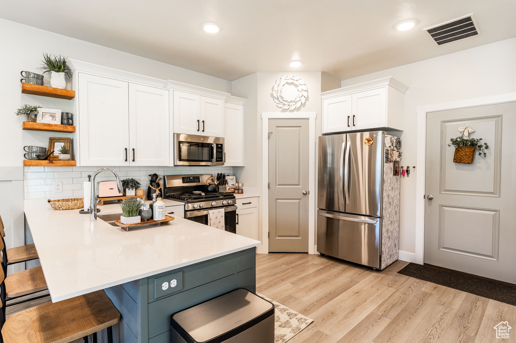 Kitchen with appliances with stainless steel finishes, a breakfast bar, open shelves, white cabinetry, and recessed lighting