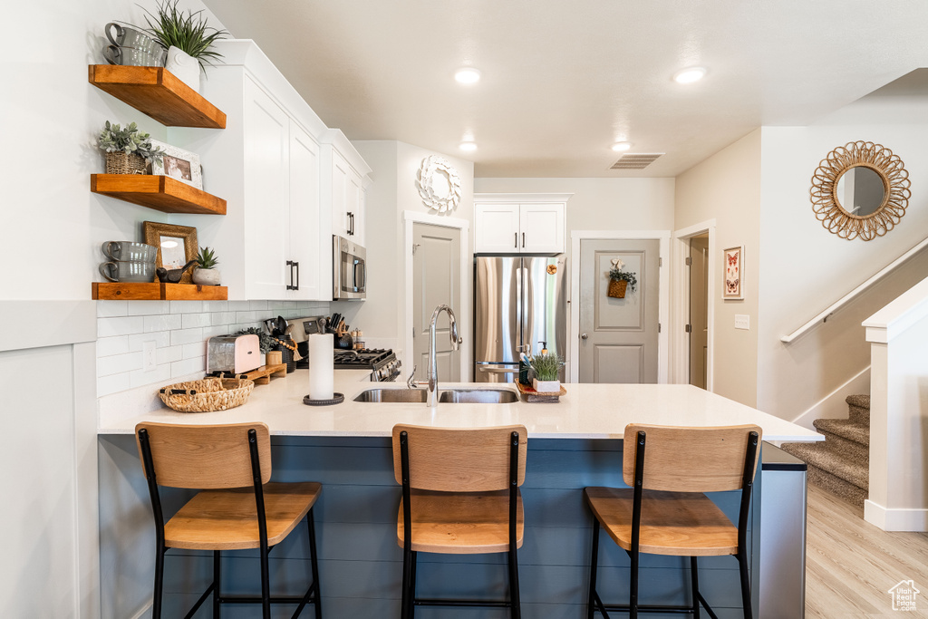 Kitchen with appliances with stainless steel finishes, open shelves, a peninsula, a sink, and white cabinets