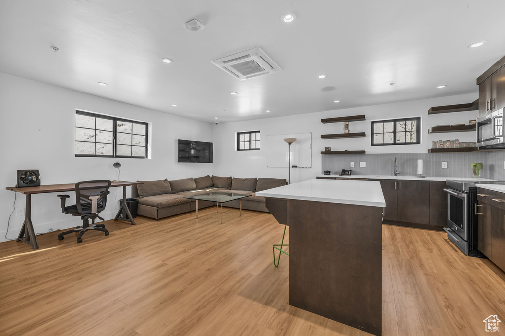 Kitchen featuring open shelves, stainless steel appliances, a kitchen island, a breakfast bar area, and light countertops