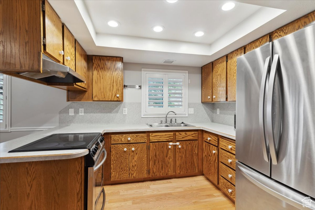 Kitchen featuring freestanding refrigerator, range with electric stovetop, a sink, brown cabinets, and recessed lighting