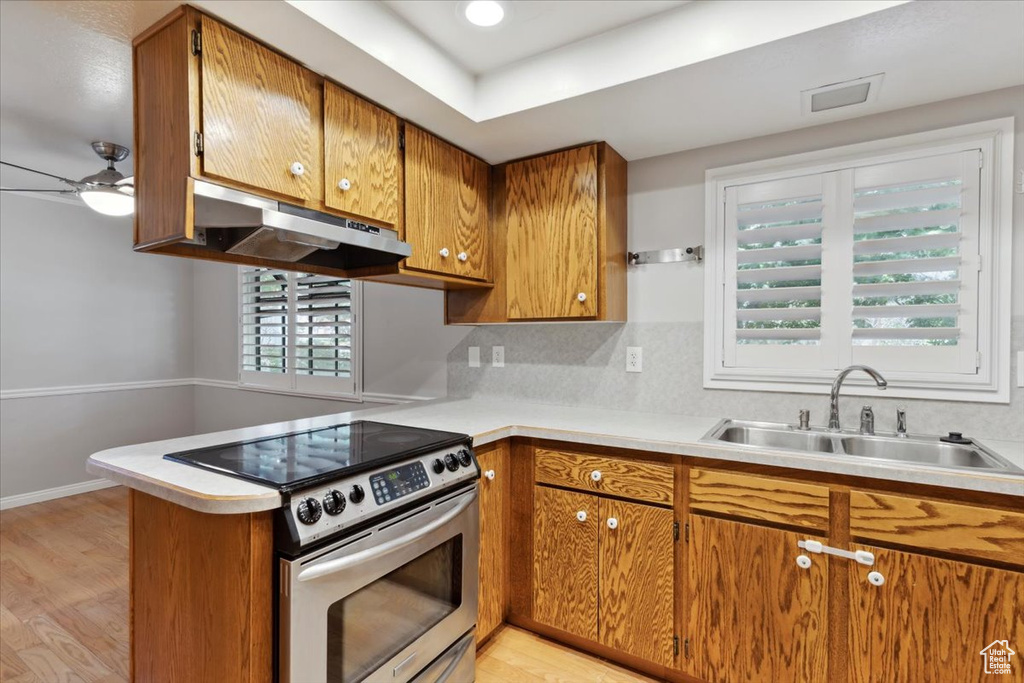 Kitchen with stainless steel range with electric stovetop, under cabinet range hood, a sink, and brown cabinetry