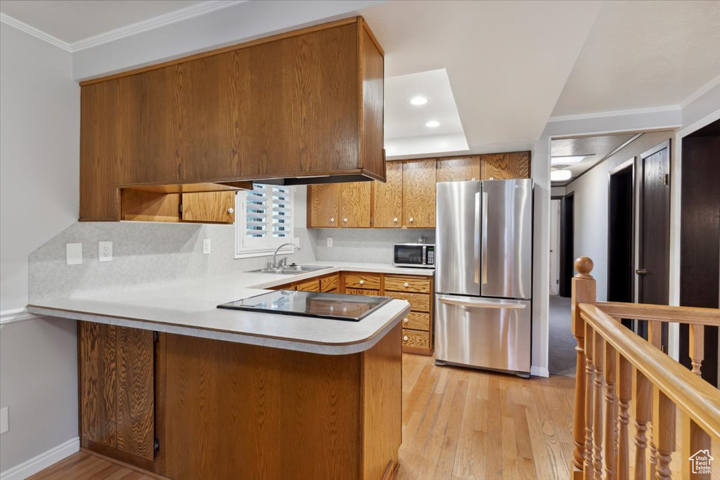 Kitchen with stainless steel appliances, a sink, light wood-style flooring, a peninsula, and decorative backsplash