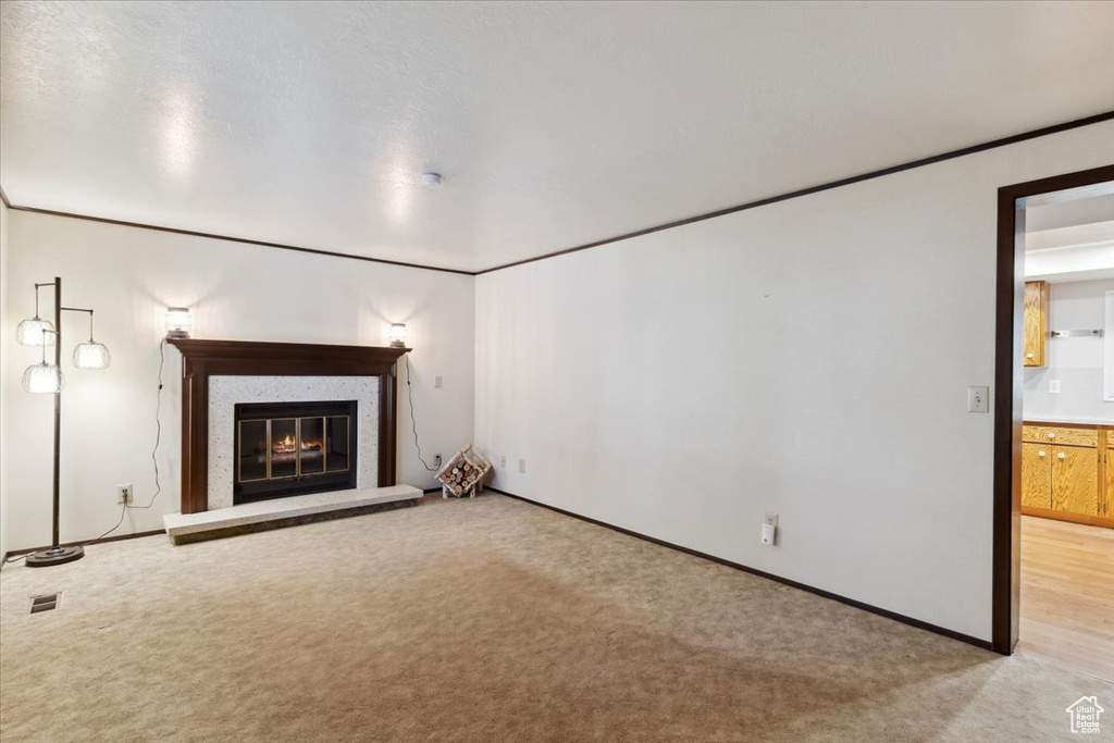 Unfurnished living room featuring light colored carpet, a glass covered fireplace, and baseboards