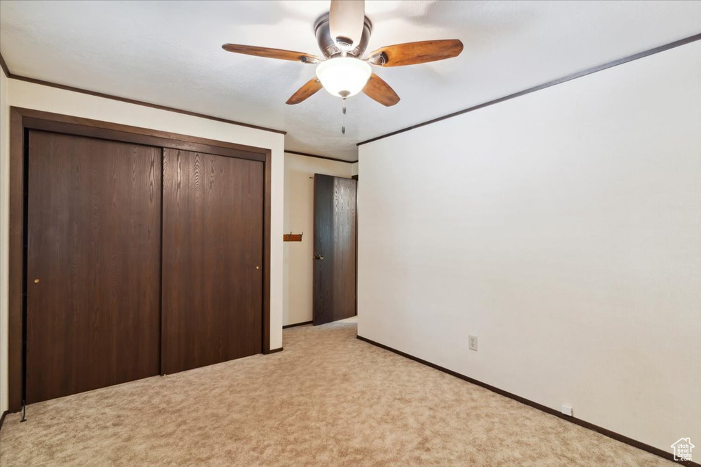 Unfurnished bedroom featuring light colored carpet, a closet, baseboards, and a ceiling fan