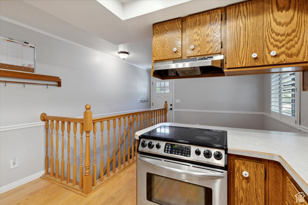 Kitchen featuring stainless steel range with electric stovetop, under cabinet range hood, light countertops, and light wood-style flooring