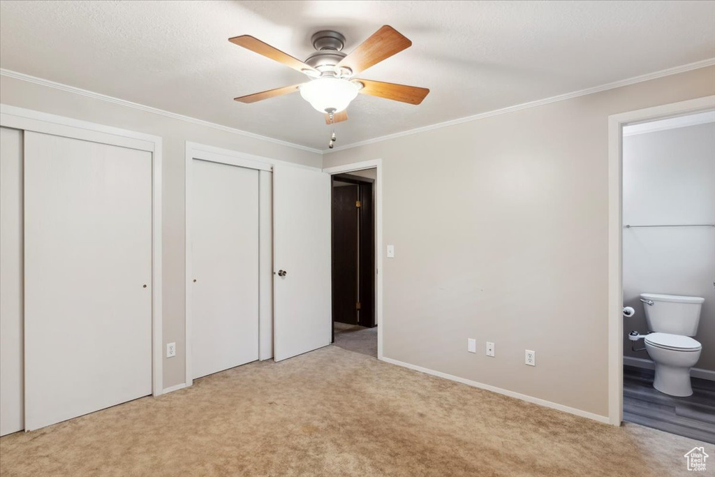 Unfurnished bedroom with two closets, carpet flooring, ensuite bathroom, ornamental molding, and baseboards