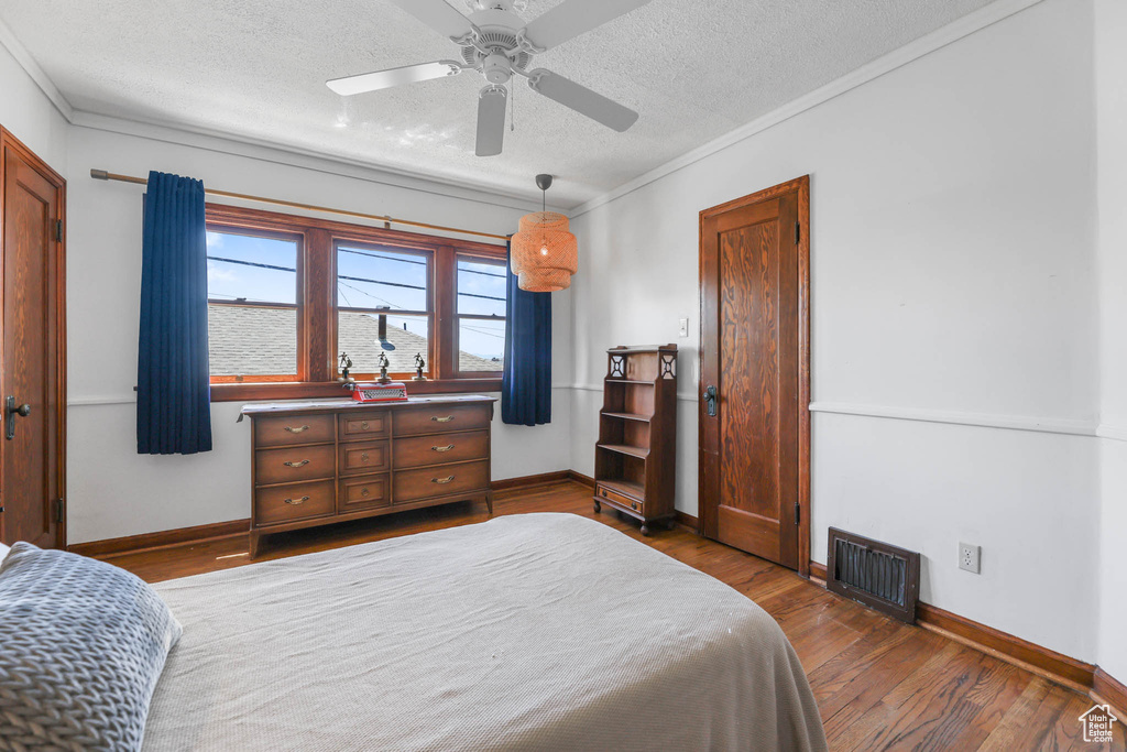 Bedroom with a textured ceiling, wood finished floors, crown molding, baseboards, and a ceiling fan