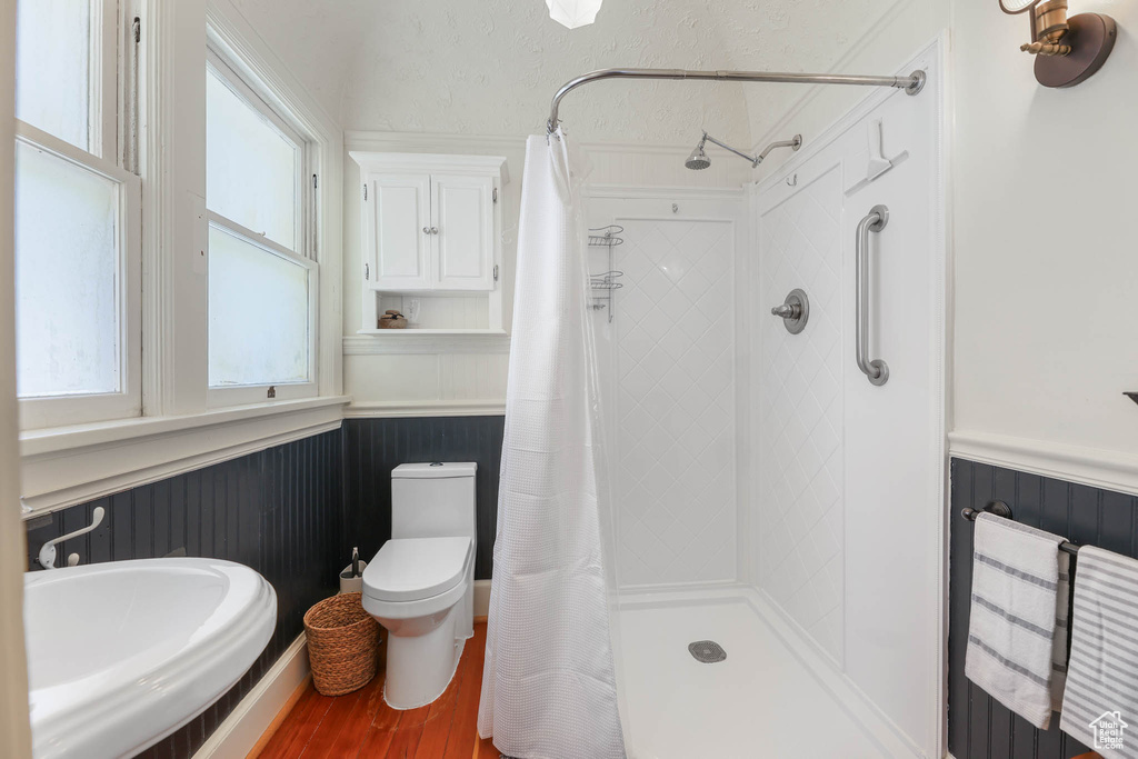 Bathroom with wainscoting, toilet, wood finished floors, and tiled shower