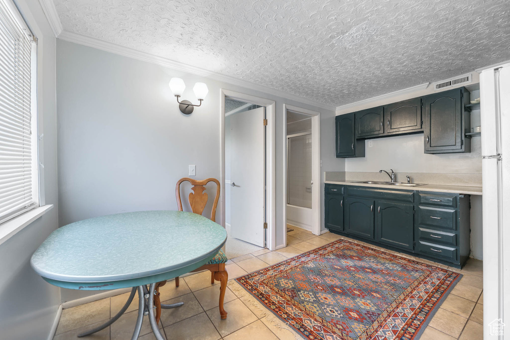 Kitchen with a sink, light countertops, crown molding, light tile patterned floors, and a textured ceiling