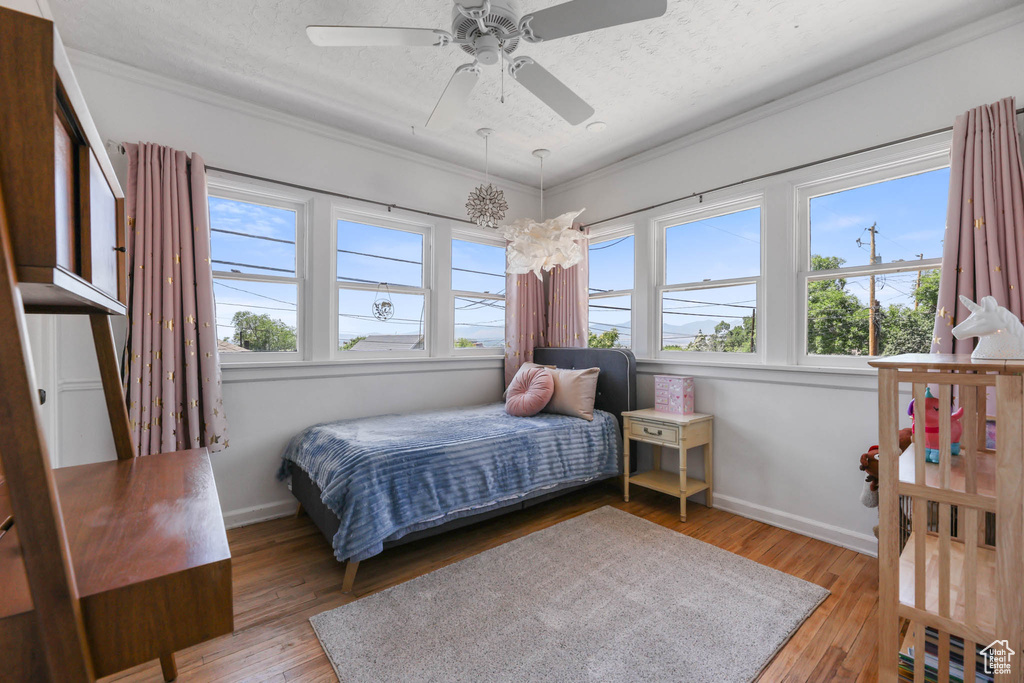 Bedroom with ornamental molding, light wood-style flooring, baseboards, ceiling fan, and a textured ceiling
