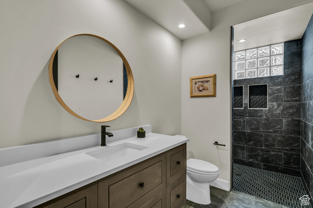 Bathroom featuring vanity, toilet, tiled shower, and recessed lighting