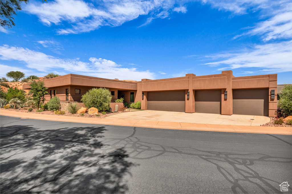 Pueblo-style house featuring stucco siding, driveway, and an attached garage