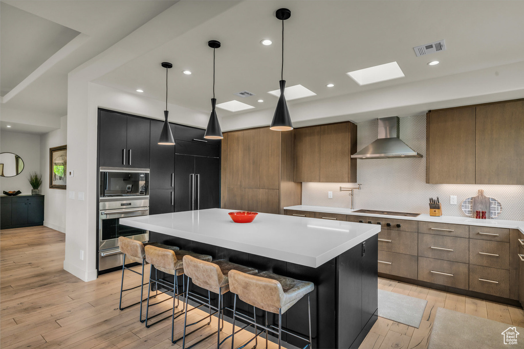 Kitchen featuring oven, wall chimney exhaust hood, light wood-type flooring, a skylight, and backsplash