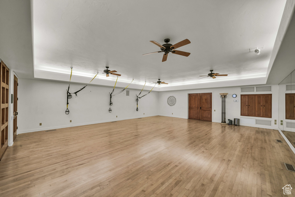Unfurnished living room with a tray ceiling, light wood-style flooring, baseboards, and a ceiling fan