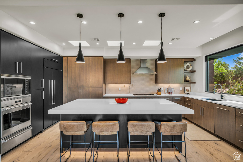 Kitchen featuring stainless steel oven, wall chimney exhaust hood, black microwave, a warming drawer, and a sink