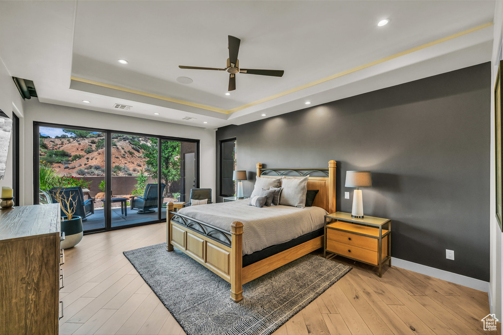 Bedroom featuring a raised ceiling, access to exterior, light wood-style floors, baseboards, and recessed lighting