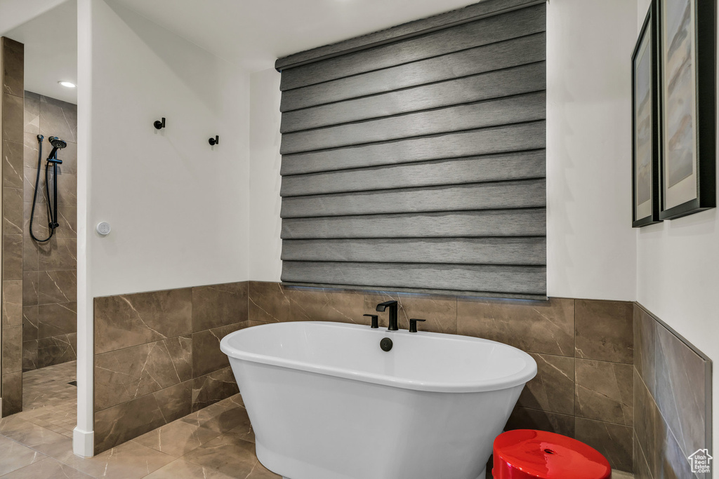 Bathroom featuring tile walls, a walk in shower, a freestanding bath, and a wainscoted wall
