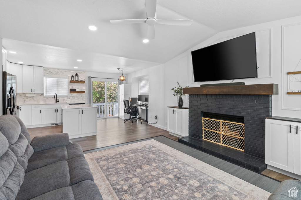 Living area featuring wood finished floors, ceiling fan, a brick fireplace, lofted ceiling, and recessed lighting