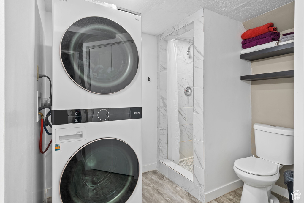 Laundry room with stacked washer and clothes dryer, wood finished floors, baseboards, and a textured ceiling
