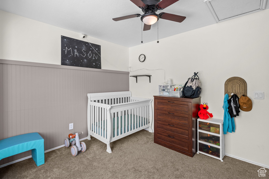 Carpeted bedroom with a crib, a ceiling fan, and baseboards