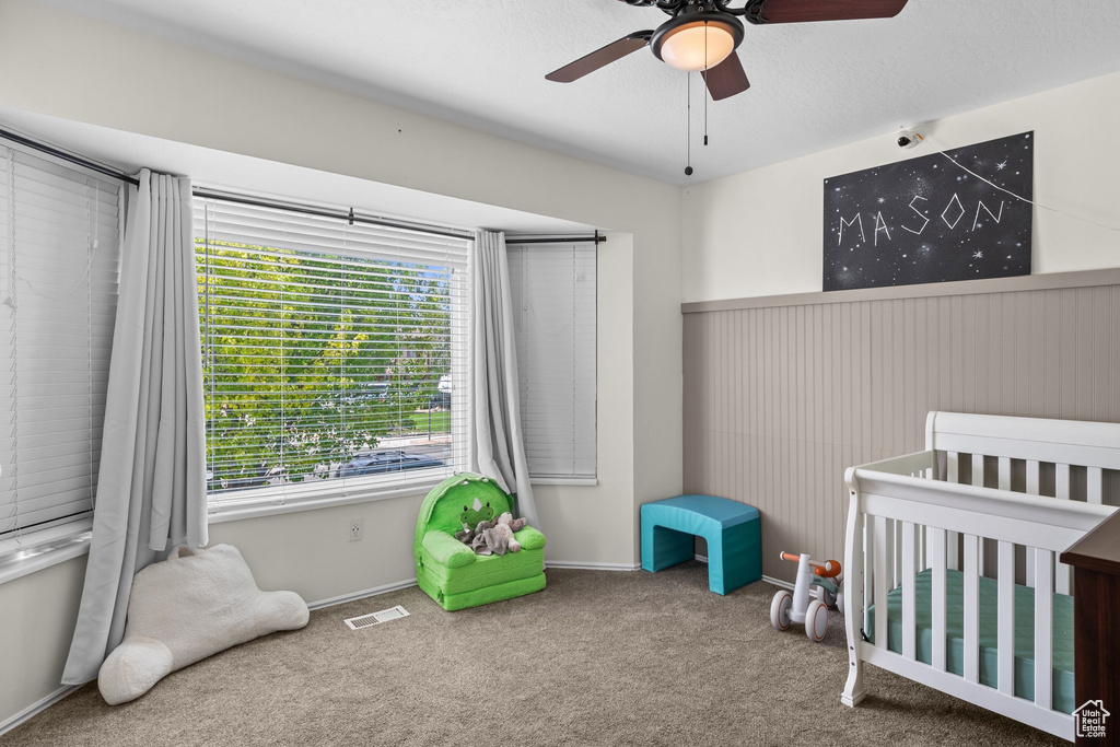 Unfurnished bedroom with a crib, carpet flooring, multiple windows, and a ceiling fan
