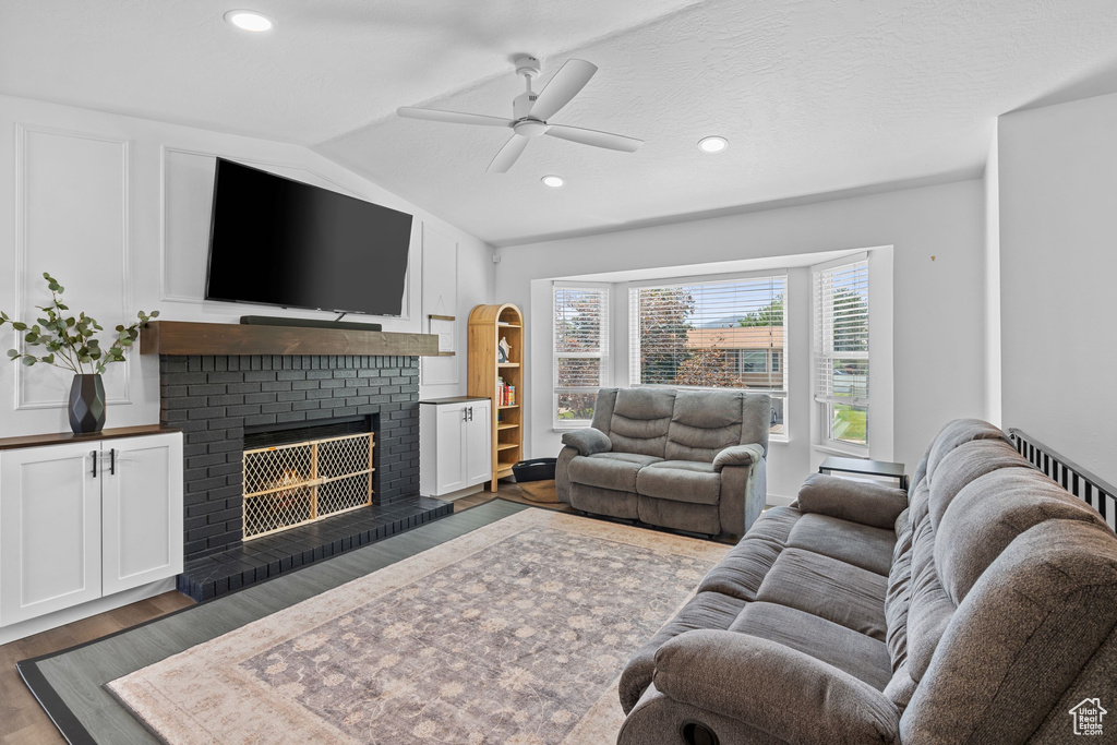 Living area with ceiling fan, dark wood finished floors, a brick fireplace, lofted ceiling, and recessed lighting