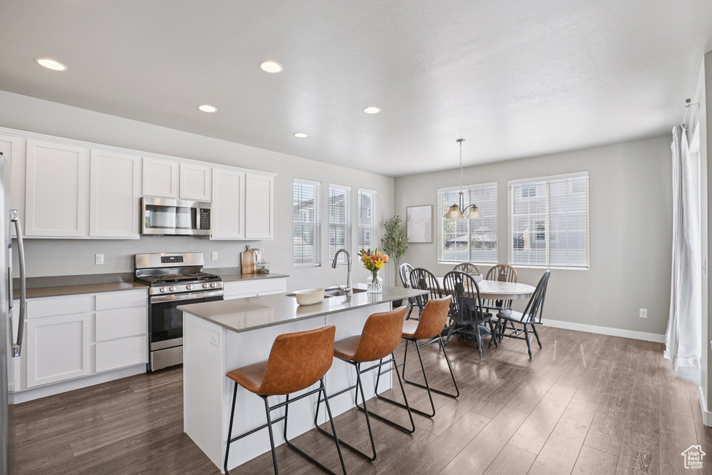 Kitchen with appliances with stainless steel finishes, a kitchen bar, dark wood finished floors, a chandelier, and recessed lighting