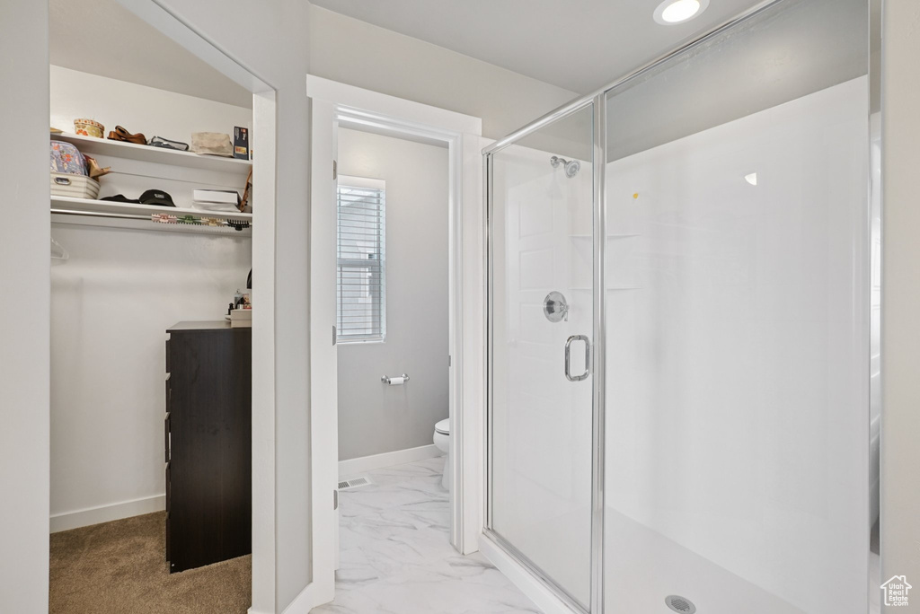 Bathroom featuring a shower stall, toilet, marble look tiles, baseboards, and a spacious closet