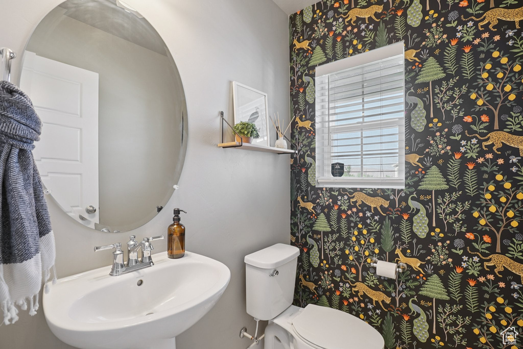 Half bathroom with a sink, wallpapered walls, and toilet