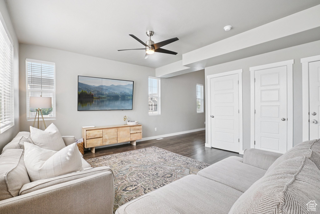 Living area with a ceiling fan, dark wood-type flooring, and baseboards