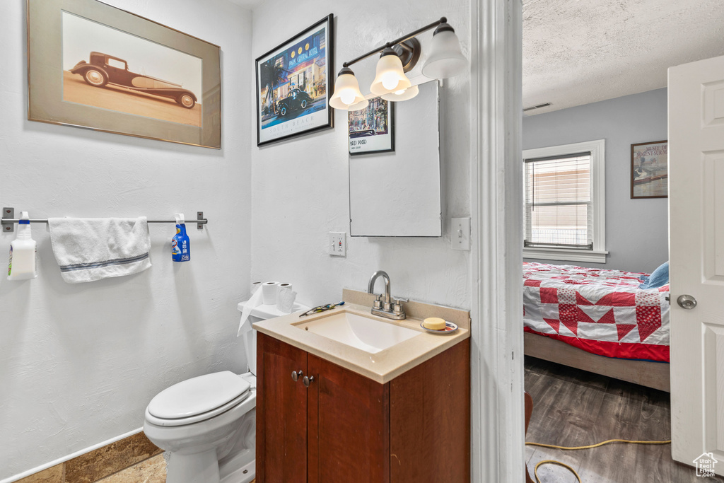 Ensuite bathroom with vanity, toilet, a textured ceiling, and baseboards