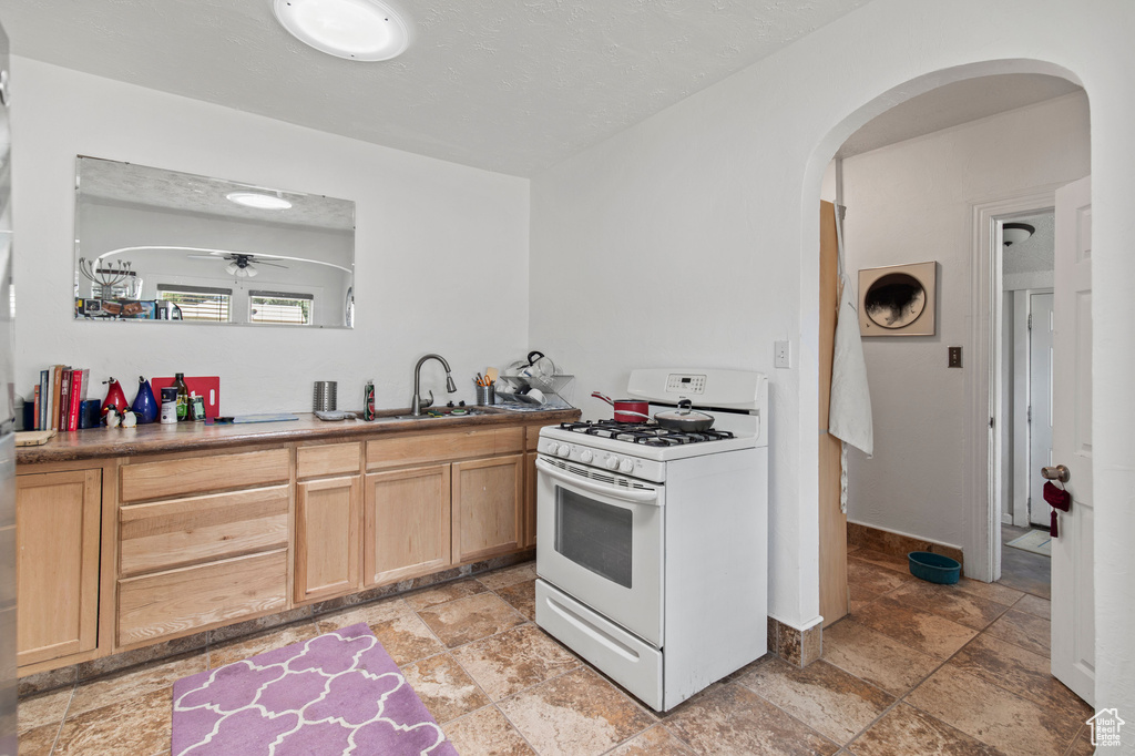 Kitchen featuring white range with gas cooktop, light brown cabinets, arched walkways, a ceiling fan, and light stone finish floors