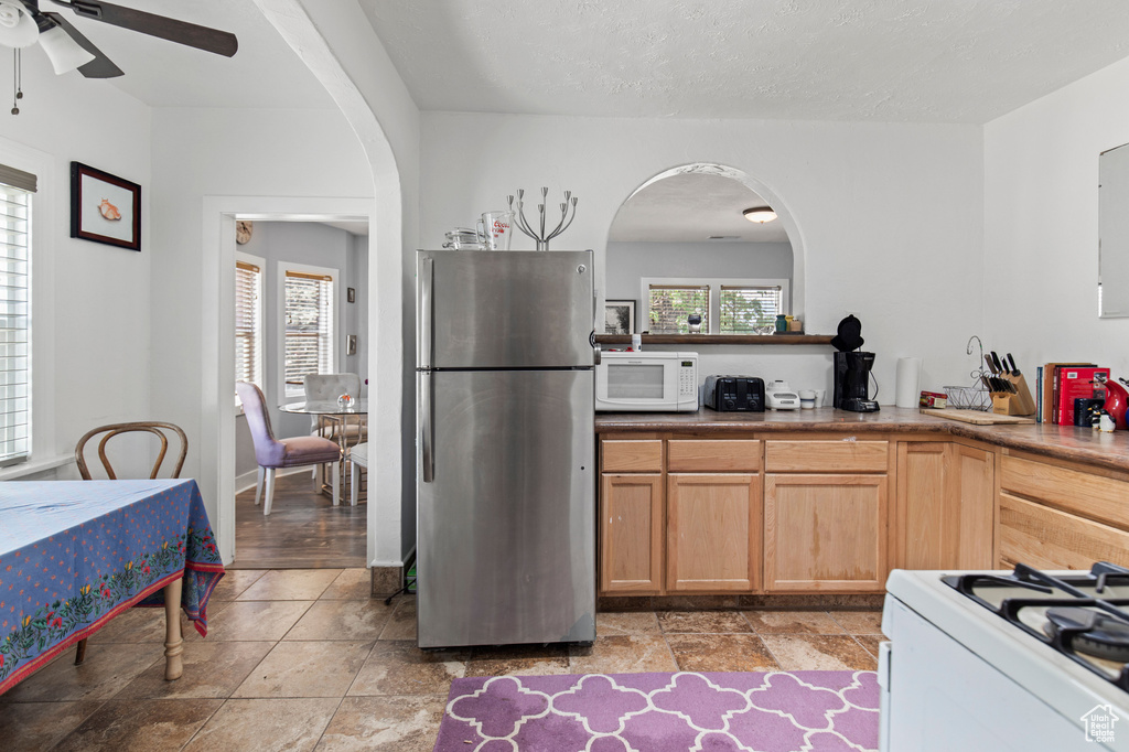 Kitchen with white appliances, arched walkways, a ceiling fan, and light brown cabinetry